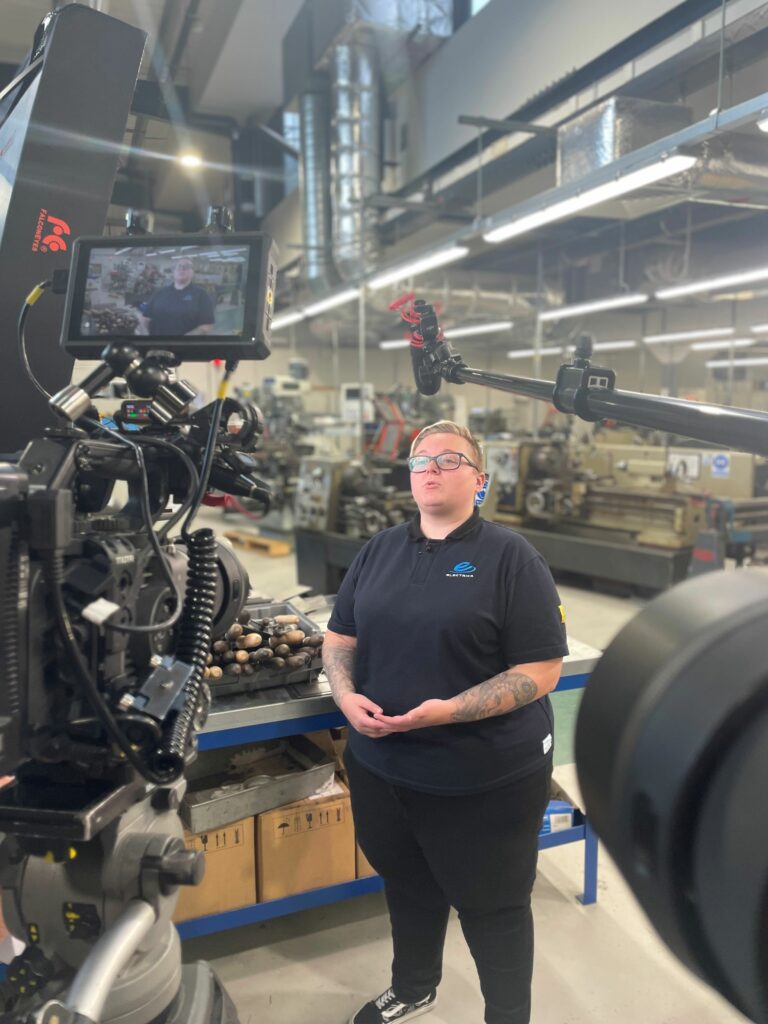 Image of Kerris standing in front of filming equipment in the engineering workshop.