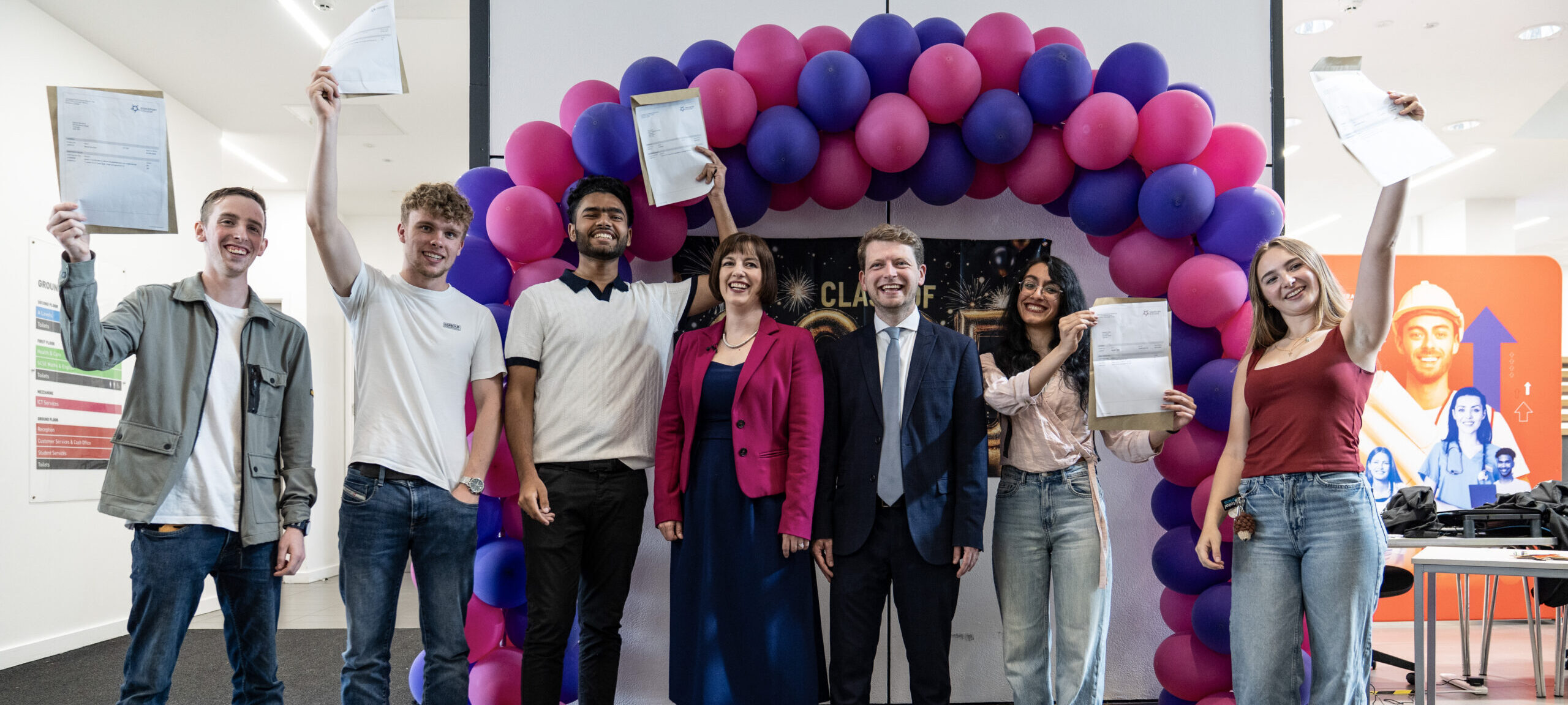 Students celebrating holding up their results in front of a balloon arch