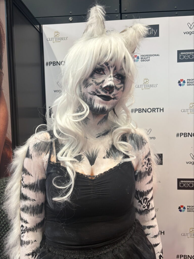 Close-up of a person in white tiger-inspired body paint with black stripes and white hair.